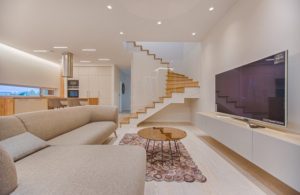 Humble abode basement family room neutral colors curved stairway big screen tv couch coffee table designer rug