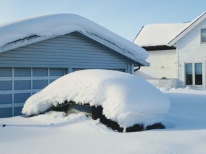 leaving winter behind at home car completely covered in snow in front of a garage