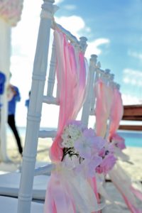 Flower wedding decor pink gauze and flowers tied to the backs of chairs for a wedding on the beach