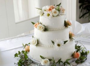 Flower wedding decor on a three layer white wedding cake garnished with roses daisies and pearls
