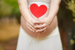 Now you are pregnant woman holding craft heart on stick