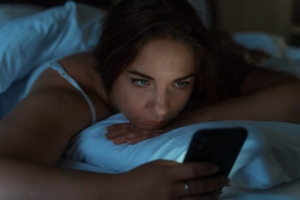 tired-young-girl-lies-in-bed-and-uses-a-smartphone