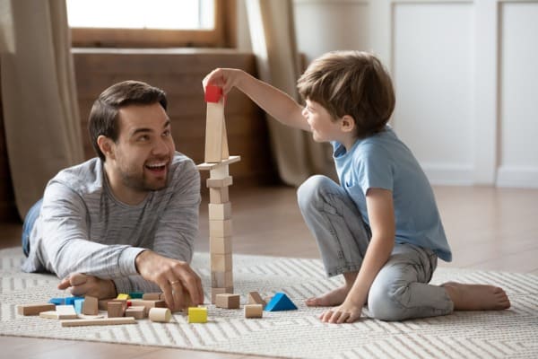 happy father playing with small schoolboy in living room