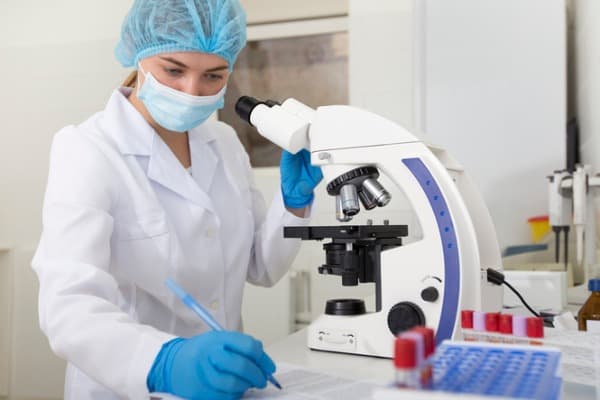 cheerful girl assistant working with microscope and writing results