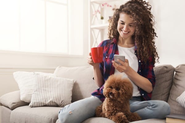 smiling young woman with mobile and little dog at home