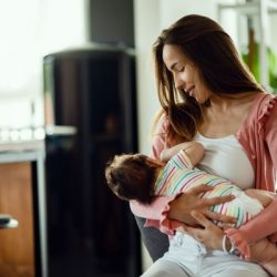 young smiling mother breastfeeding her baby at home