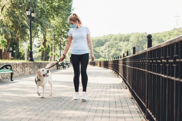 blonde woman and her dog walking in the park while wearing a medical mask