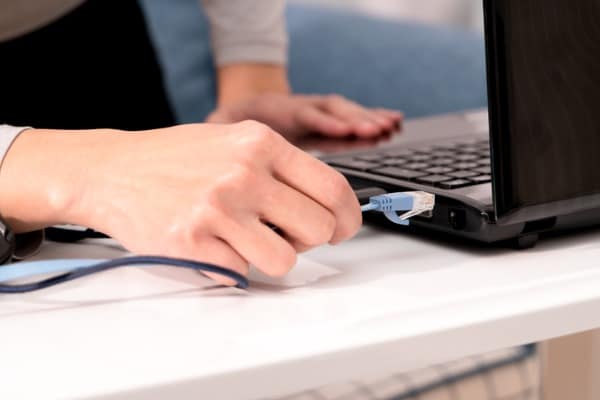 women hand is plugging in the lan cable to laptop port